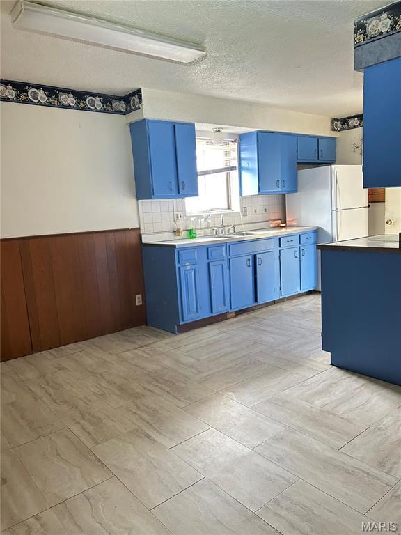 3757 Itaska St, Saint Louis, MO 63116 - kitchen with blue cabinets, a wainscoted wall, light countertops, wood walls, and decorative backsplash