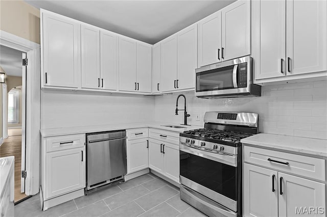 2220 Nebraska Ave, Saint Louis, MO 63104 - kitchen with stainless steel appliances, a sink, white cabinets, light tile patterned flooring, and decorative backsplash