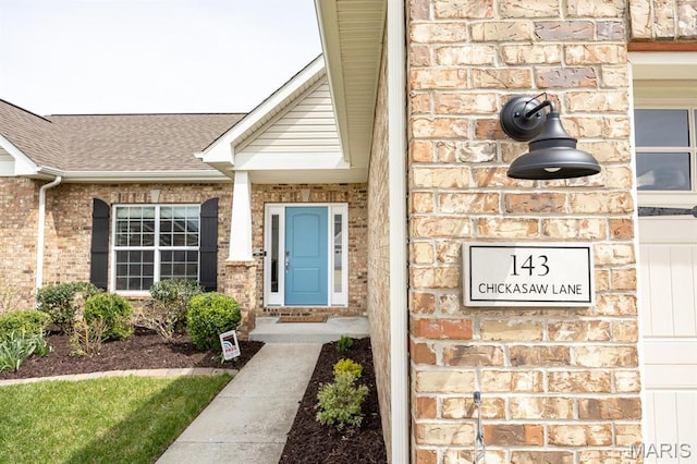 view of exterior entry featuring brick siding and a shingled roof