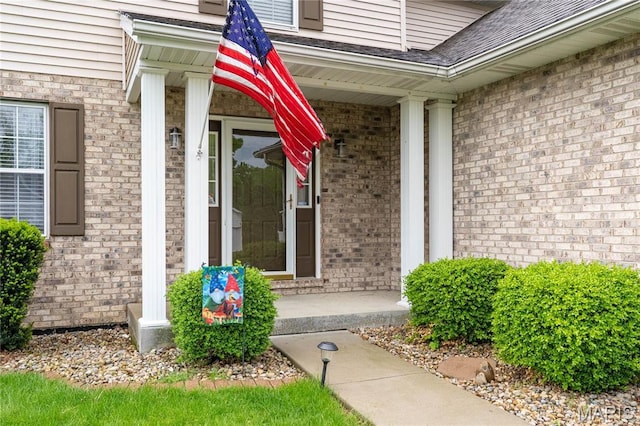 entrance to property featuring a porch and brick siding