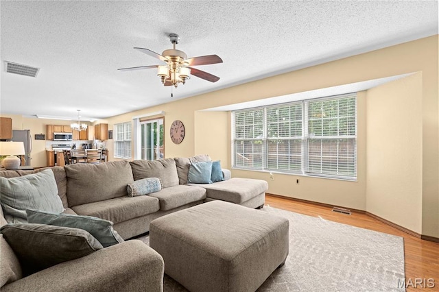 living room with a chandelier, ceiling fan, light wood-style flooring, a textured ceiling, and baseboards