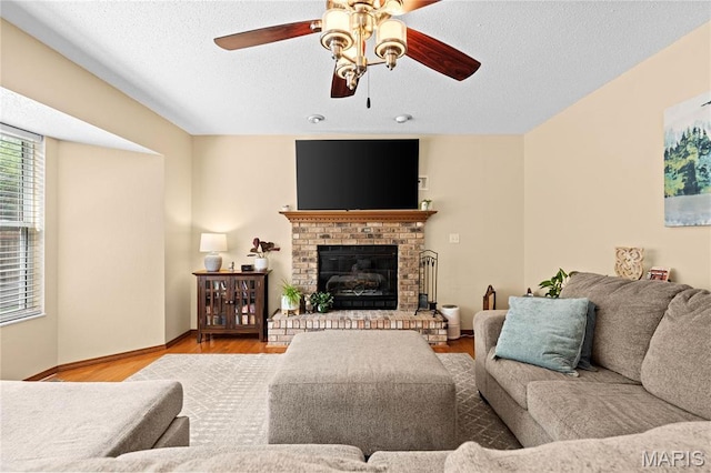 living area featuring a ceiling fan, wood finished floors, a brick fireplace, baseboards, and a textured ceiling