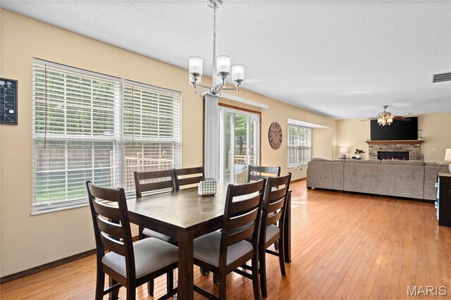 dining room with a chandelier, a ceiling fan, light wood-type flooring, a textured ceiling, and a warm lit fireplace