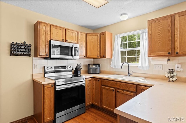 kitchen with stainless steel appliances, a sink, light countertops, a textured ceiling, and decorative backsplash