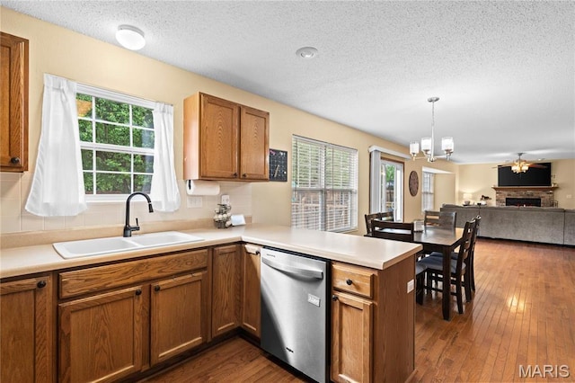 kitchen with dishwasher, a sink, a textured ceiling, a peninsula, and brown cabinets
