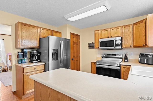 kitchen featuring appliances with stainless steel finishes, a sink, light wood-style flooring, tasteful backsplash, and light countertops
