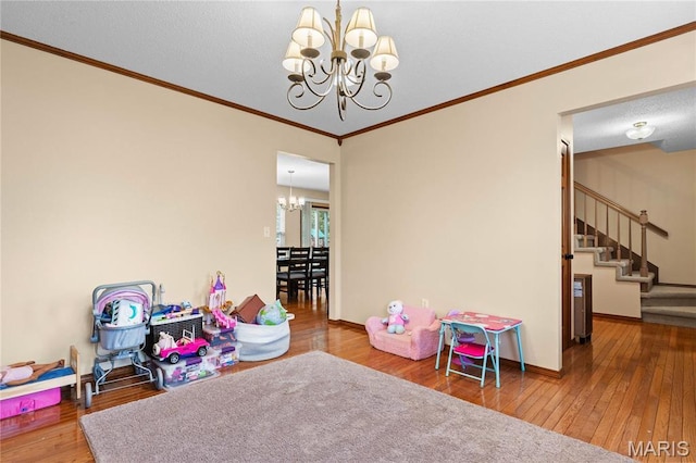 playroom featuring a chandelier, hardwood / wood-style flooring, ornamental molding, and baseboards