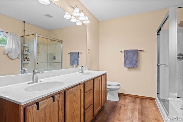 bathroom featuring wood finished floors, a stall shower, double vanity, and toilet