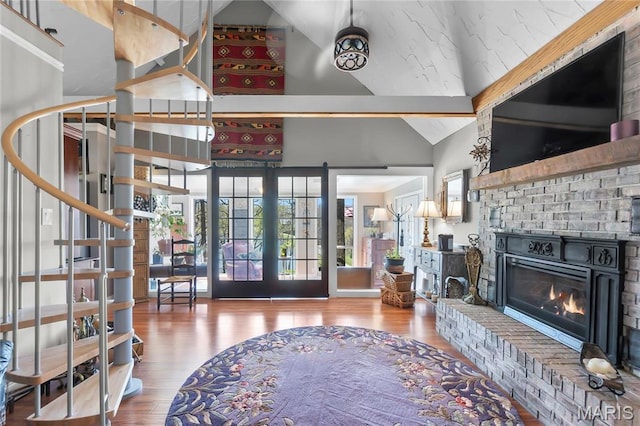 living area with high vaulted ceiling, wood finished floors, stairway, a brick fireplace, and french doors