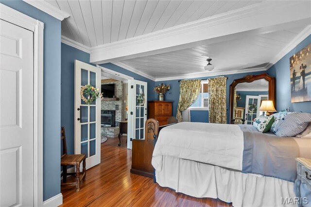 bedroom with wood finished floors, ornamental molding, and a stone fireplace