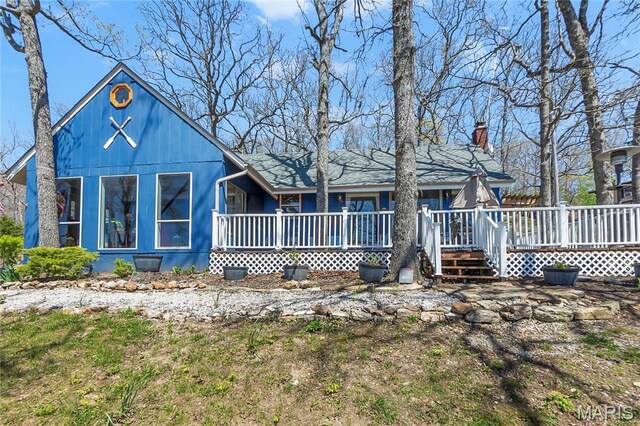 back of property with a chimney, covered porch, and a wooden deck