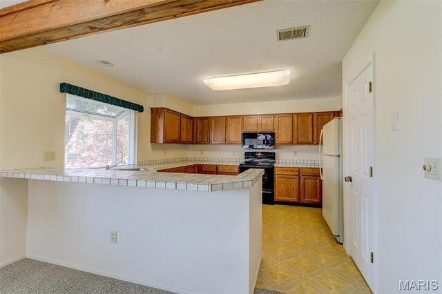228 Hemingway Ln Unit F, Weldon Spring, MO 63304 - kitchen featuring black electric range oven, freestanding refrigerator, a peninsula, brown cabinetry, and tile countertops