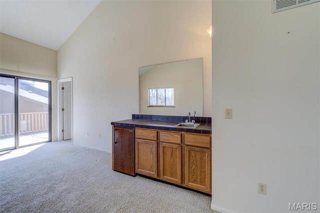 228 Hemingway Ln Unit F, Weldon Spring, MO 63304 - kitchen featuring a sink, tile countertops, brown cabinetry, light carpet, and high vaulted ceiling