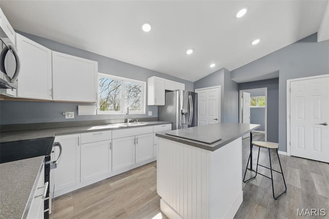 kitchen featuring stainless steel refrigerator with ice dispenser, range with electric stovetop, a sink, vaulted ceiling, and a kitchen island