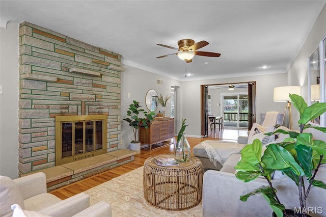 living room featuring ceiling fan, wood finished floors, and a stone fireplace