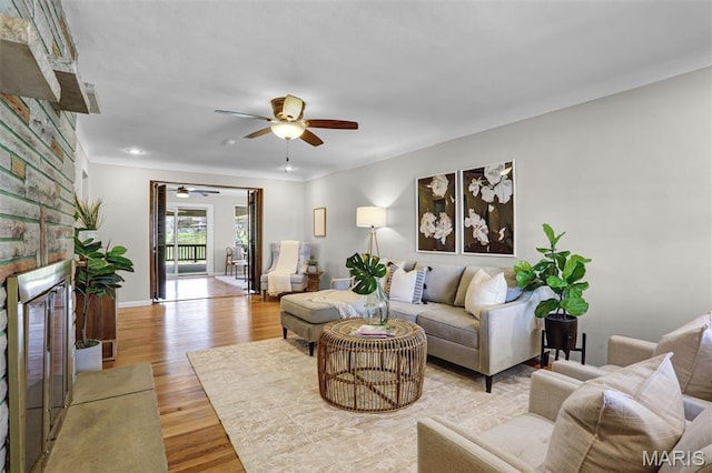 living area with a fireplace, a ceiling fan, wood finished floors, baseboards, and ornamental molding