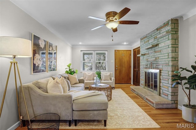 living area with a fireplace, a ceiling fan, wood finished floors, and baseboards
