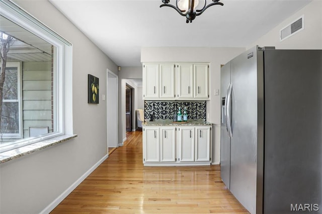 kitchen with stainless steel fridge with ice dispenser, white cabinets, light wood-style floors, a chandelier, and baseboards