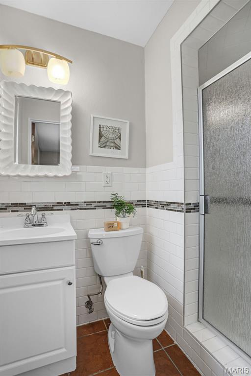 bathroom with a stall shower, tile patterned floors, toilet, vanity, and a wainscoted wall