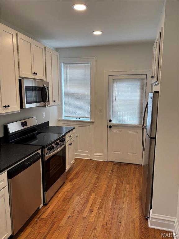 4519 Flora Ave, Saint Louis, MO 63110 - kitchen featuring appliances with stainless steel finishes, dark countertops, light wood-style flooring, white cabinets, and recessed lighting