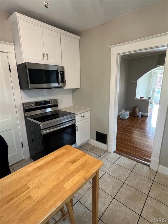 2326 Patton Ave, Saint Louis, MO 63144 - kitchen featuring appliances with stainless steel finishes, light tile patterned floors, white cabinetry, and arched walkways
