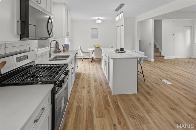 kitchen featuring stainless steel appliances, a sink, a kitchen breakfast bar, light wood-type flooring, and white cabinetry