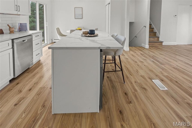 kitchen featuring dishwasher, a kitchen bar, light wood-type flooring, and white cabinetry
