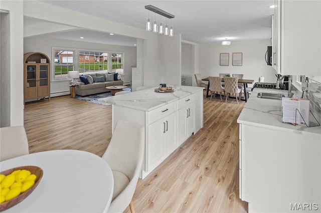 kitchen with open floor plan, white cabinets, light wood-style floors, light stone counters, and pendant lighting