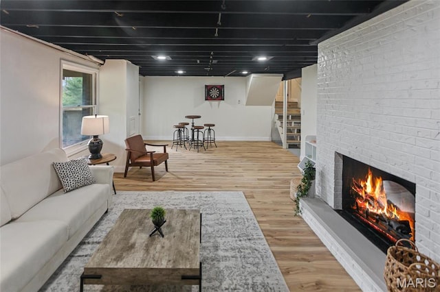 living area with stairway, baseboards, wood finished floors, and a brick fireplace