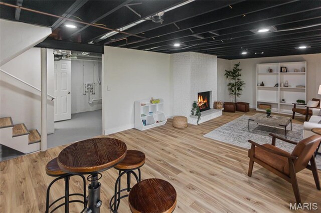 living room featuring stairway, a brick fireplace, wood finished floors, and baseboards