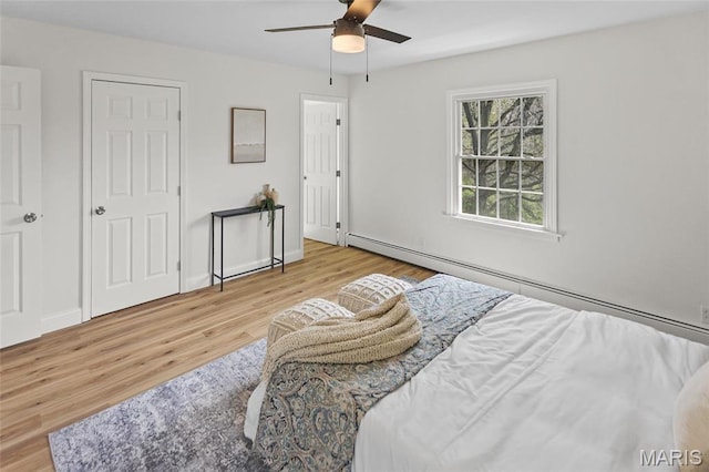 bedroom featuring wood finished floors, a baseboard heating unit, ceiling fan, and baseboards
