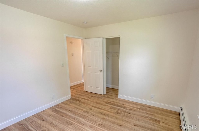 unfurnished bedroom with a baseboard radiator, light wood-style flooring, baseboards, and a closet