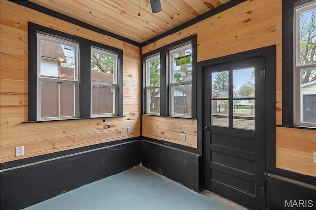 doorway featuring wood walls, plenty of natural light, concrete flooring, and wooden ceiling