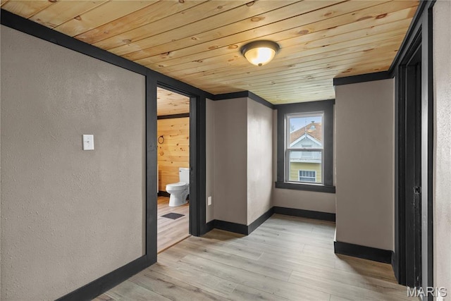 empty room with wooden ceiling, light wood finished floors, baseboards, and a textured wall