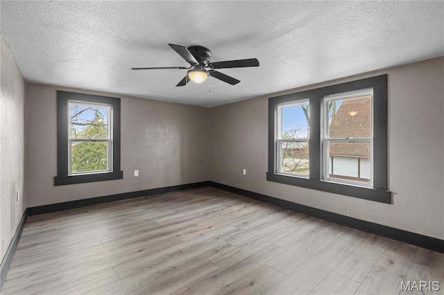 empty room with a textured ceiling, light wood-style flooring, a ceiling fan, and baseboards