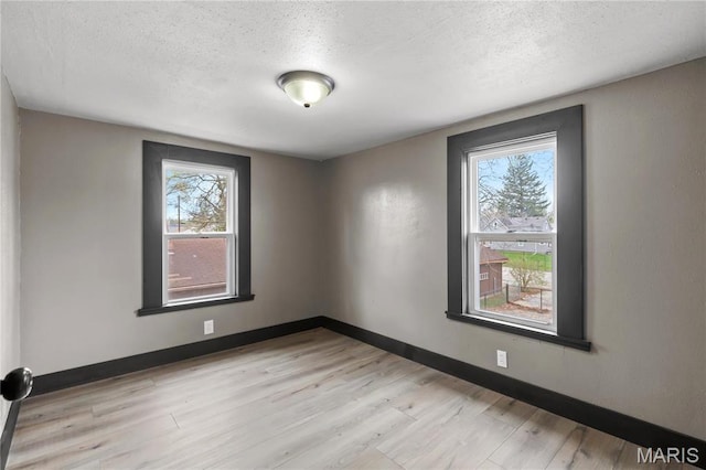 empty room featuring a textured ceiling, light wood-style flooring, and baseboards