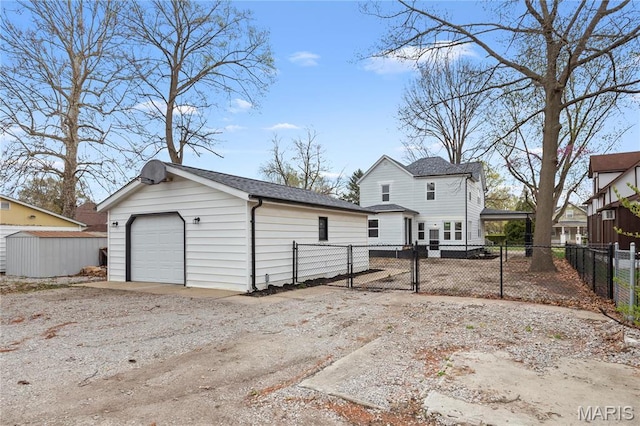 back of property featuring an outdoor structure, a garage, fence, driveway, and a shingled roof