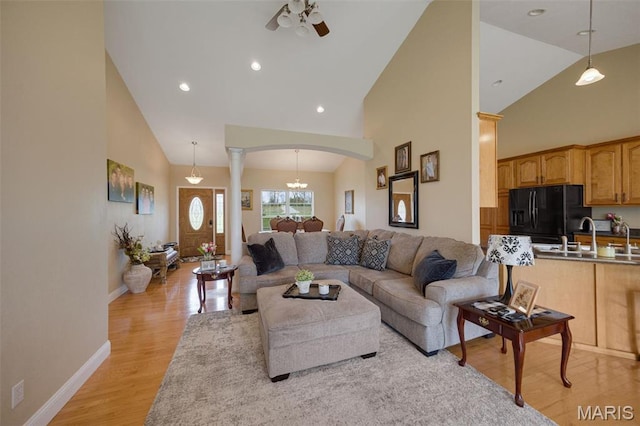 living room with arched walkways, ceiling fan, light wood-style floors, ornate columns, and high vaulted ceiling