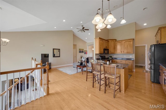 kitchen with a chandelier, black appliances, a kitchen breakfast bar, baseboards, and high vaulted ceiling