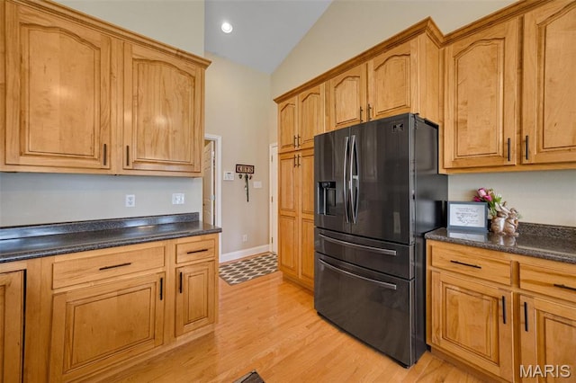 kitchen with black fridge, dark countertops, light wood finished floors, lofted ceiling, and brown cabinets