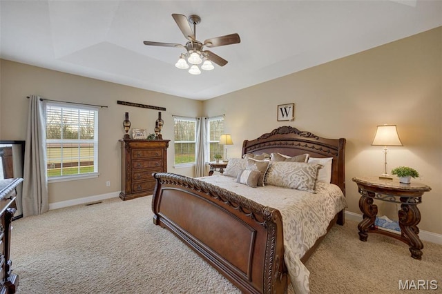 bedroom featuring light carpet, baseboards, ceiling fan, and a raised ceiling