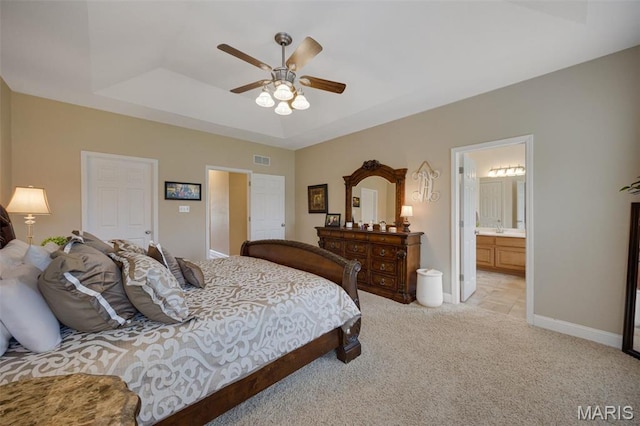 bedroom featuring light colored carpet, baseboards, a raised ceiling, and ensuite bath