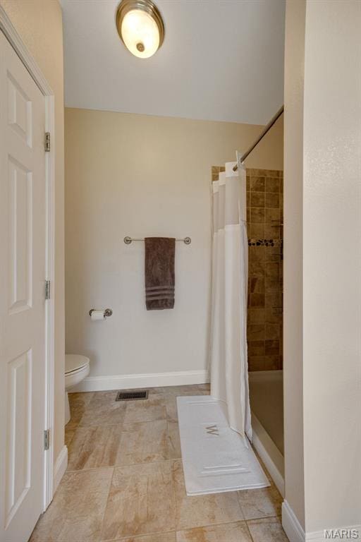 bathroom with a tile shower, toilet, baseboards, and tile patterned flooring