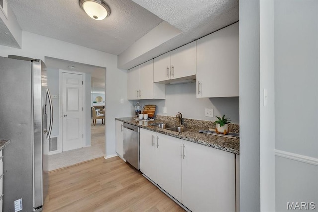 kitchen featuring appliances with stainless steel finishes, a sink, white cabinetry, light wood-style floors, and dark stone countertops
