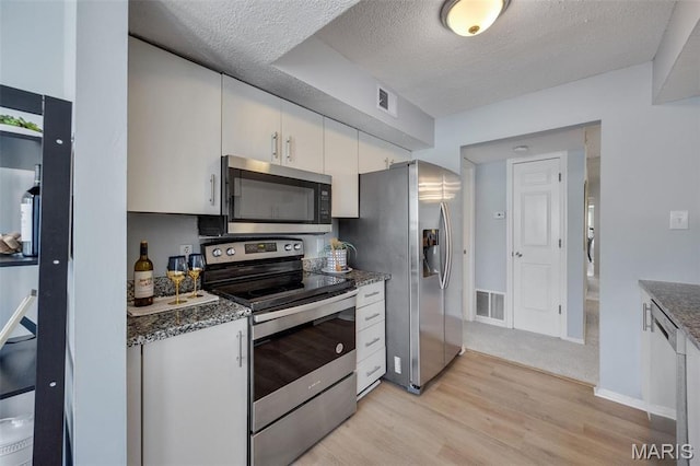 kitchen featuring stainless steel appliances, light wood-style floors, white cabinetry, a textured ceiling, and dark stone counters