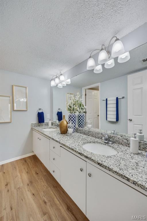 full bath featuring wood finished floors, a textured ceiling, baseboards, and double vanity