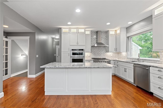 809 Star Ridge Ct, Defiance, MO 63341 - kitchen featuring appliances with stainless steel finishes, wall chimney range hood, decorative backsplash, a kitchen island, and light wood-type flooring