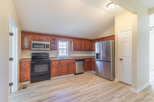 kitchen featuring appliances with stainless steel finishes, light wood-style flooring, vaulted ceiling, glass insert cabinets, and a sink