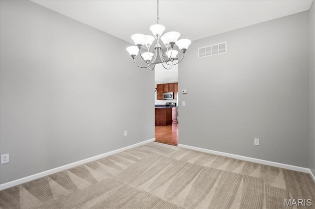 empty room featuring a chandelier, light carpet, and baseboards
