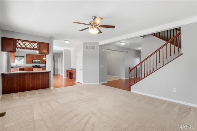 unfurnished living room featuring light carpet, ceiling fan, baseboards, and stairs
